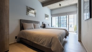 Un dormitorio moderno con una cama grande, una mesita de noche pequeña y un ventanal con vistas a la ciudad.