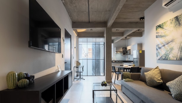 Una sala de estar moderna con televisor de pantalla plana, sofá, una mesa de centro y un área de comedor al fondo.