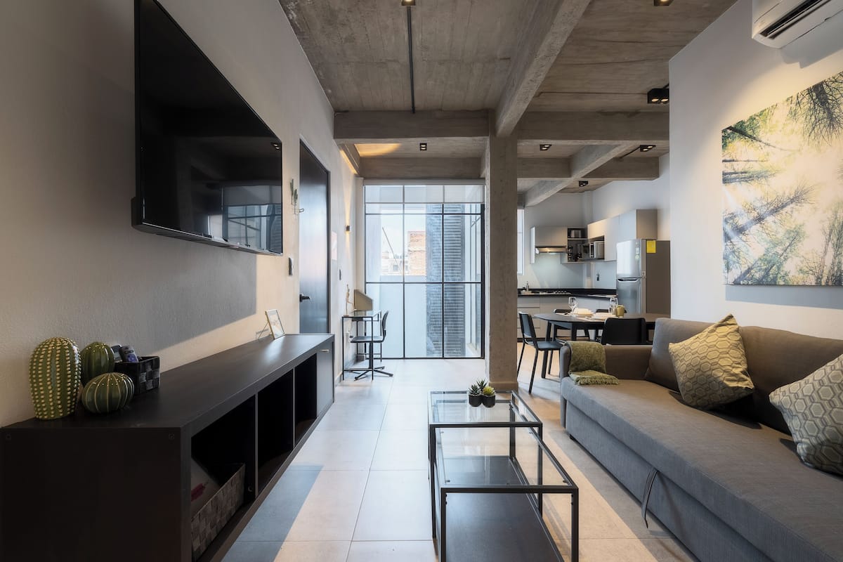 A modern living room with a flat-screen TV, a sofa, a coffee table, and a dining area in the background.