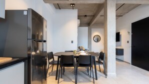 Una cocina moderna con un refrigerador de acero inoxidable, una mesa de comedor con sillas y un espejo redondo en la pared.
