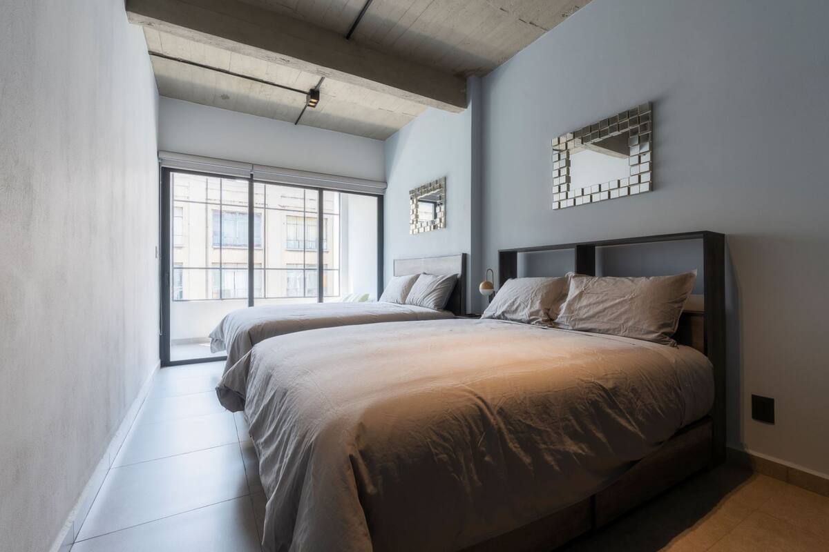 A modern bedroom with two beds, a large window, and a concrete ceiling.