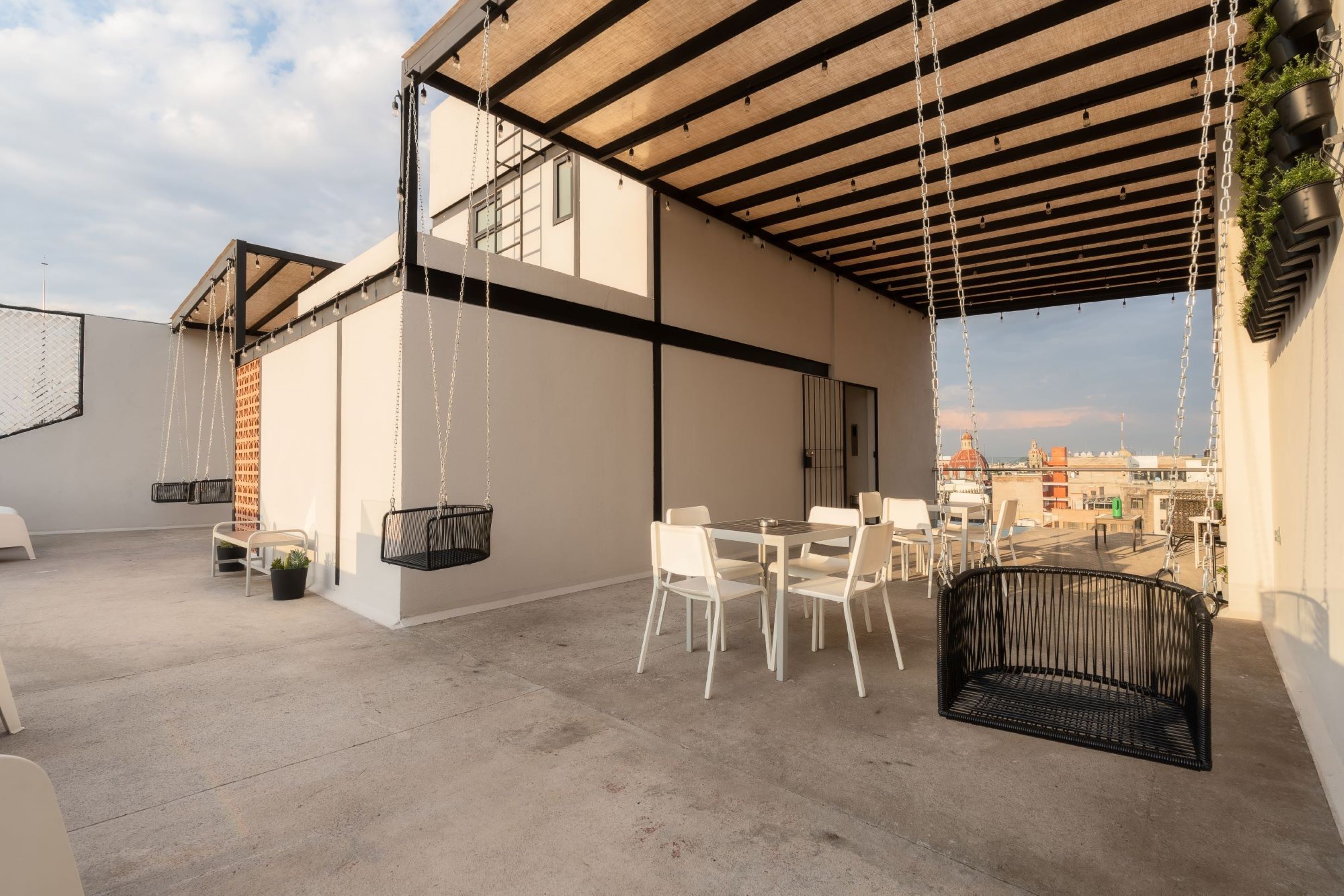 A rooftop terrace with a dining area, hanging chairs, and a black bench.