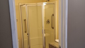 A glass-enclosed shower stall with a white door and a handrail. - Southern Comfort Hotel (Tulsa)