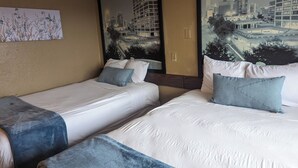 A hotel room with two beds, a large mirror, and a cityscape mural on the wall. - Southern Comfort Hotel (Tulsa)