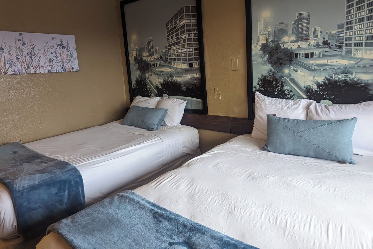 A hotel room with two beds, a large mirror, and a cityscape mural on the wall.