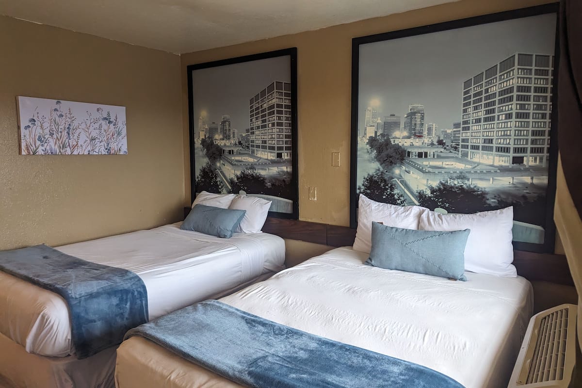 A hotel room with two beds, beige walls, and large cityscape murals.