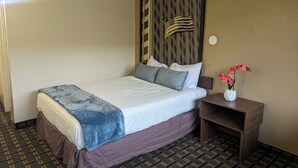 A hotel room with a bed, a nightstand with a vase of flowers, and a wall with a decorative panel. - Southern Comfort Hotel (Tulsa)