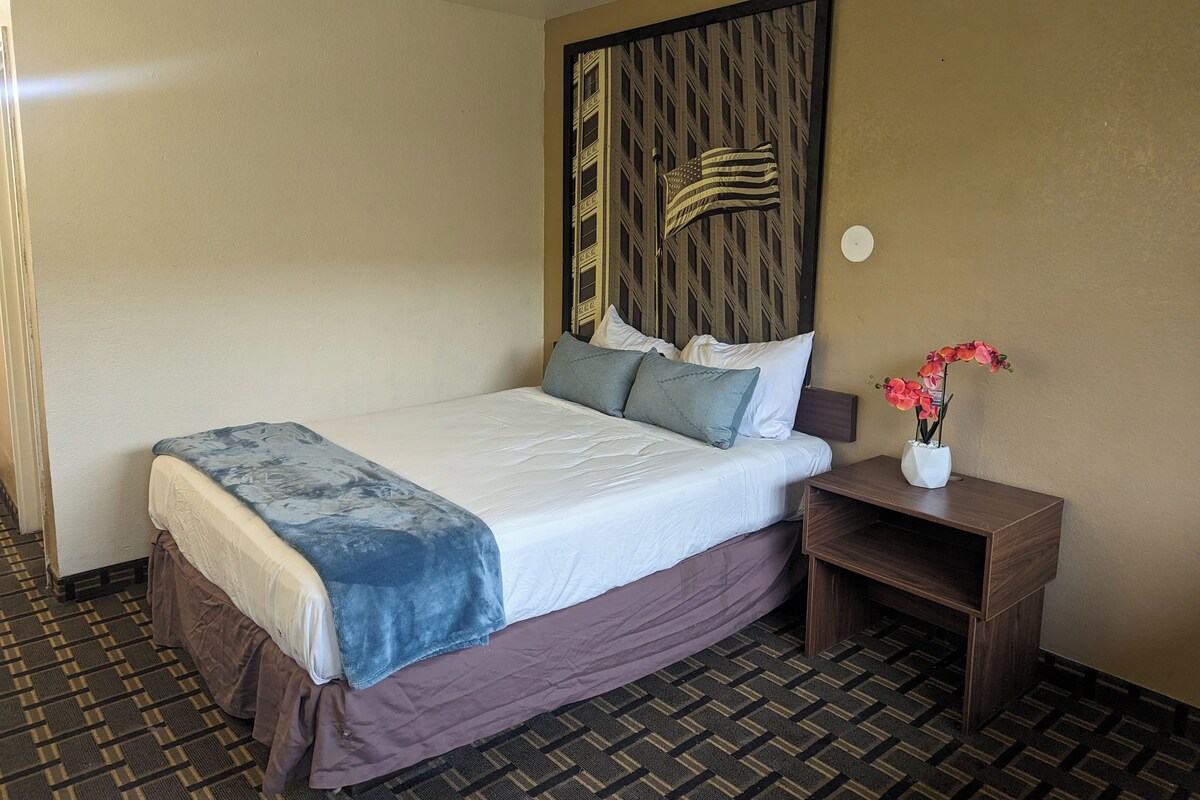 A hotel room with a bed, a nightstand with a vase of flowers, and a wall with a decorative panel.