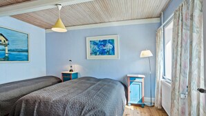 Ein Schlafzimmer mit zwei Betten, einem Gemälde, einer Lampe und einem Fenster mit Vorhängen.