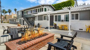 A modern outdoor patio area with a brick fire pit, outdoor seating, and a pergola. - Entire Complex | Steps To The Sand | Sleeps 20 (Huntington Beach)
