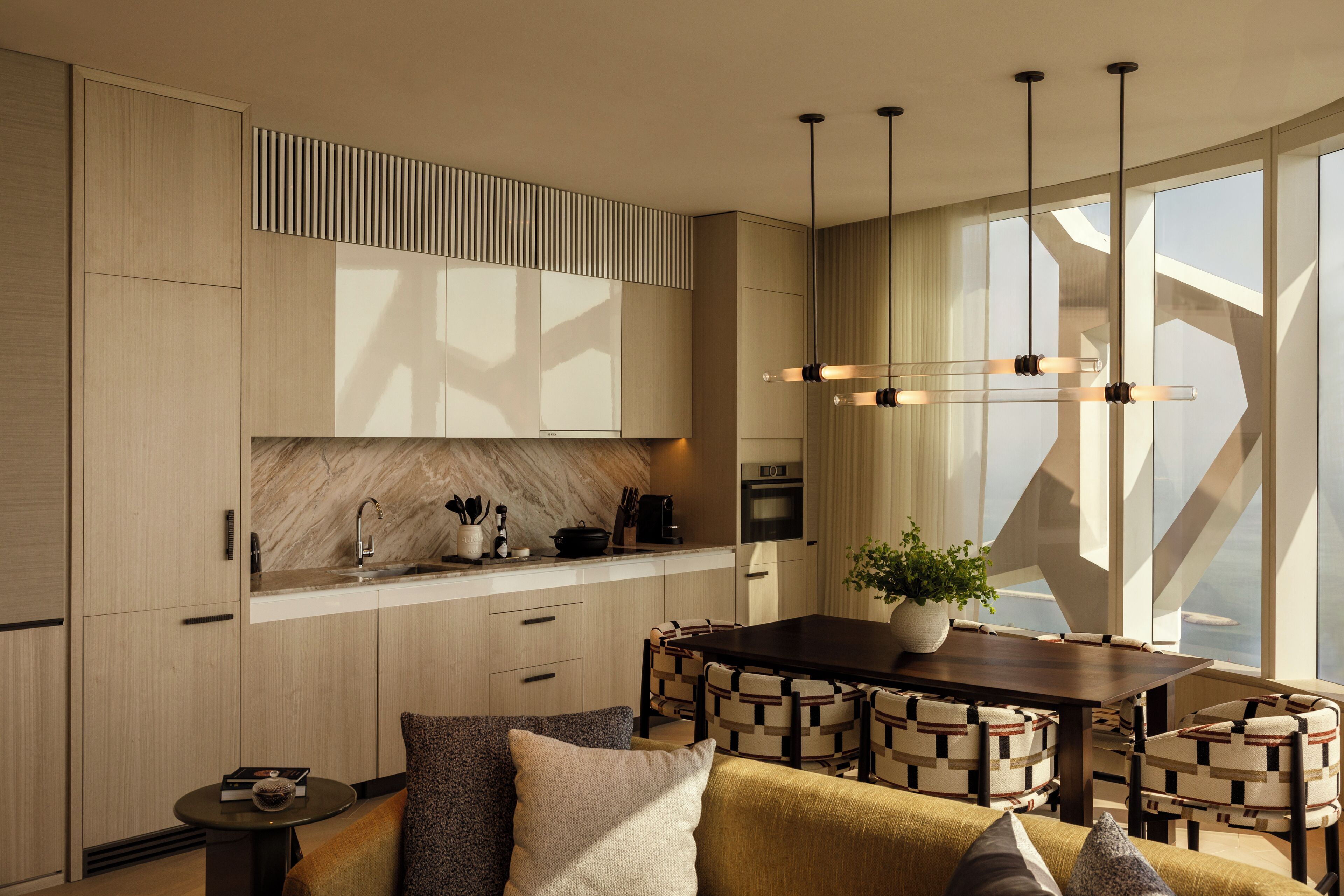 A modern kitchen with a marble countertop, wooden cabinets, and a dining area with a dark wooden table and patterned chairs.