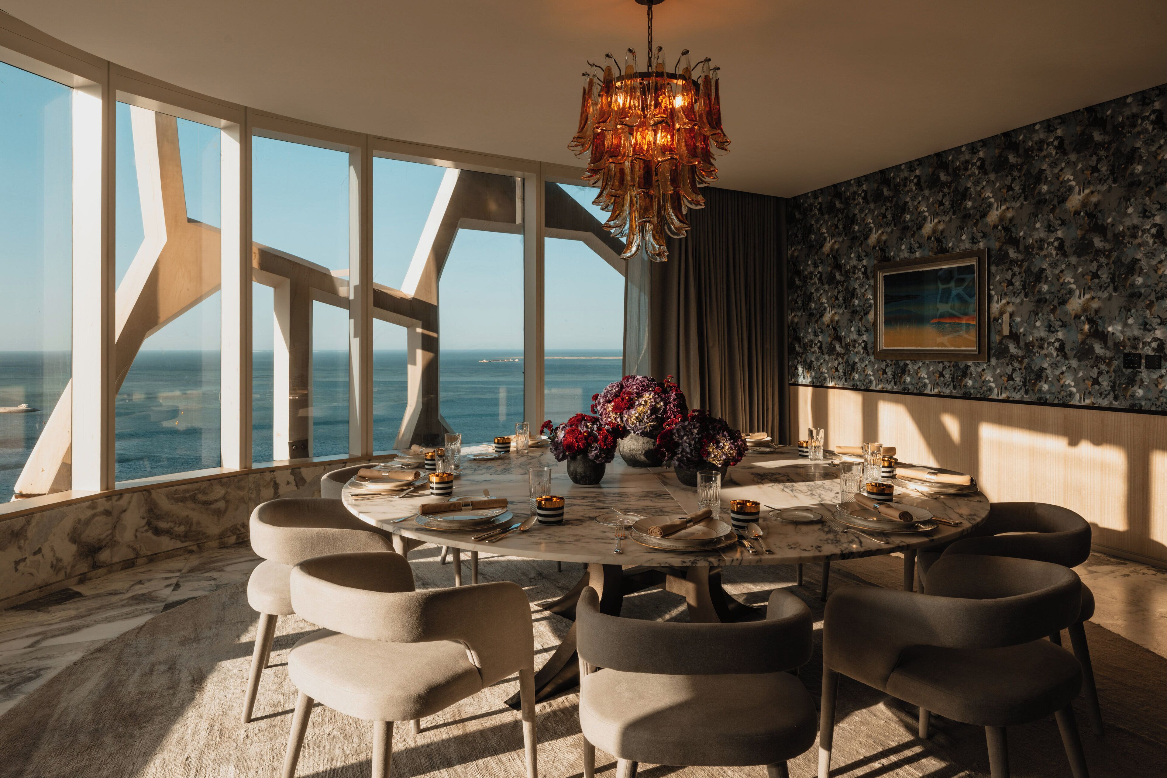 Una sala da pranzo con un tavolo grande, sedie, un lampadario e vista sull'oceano.