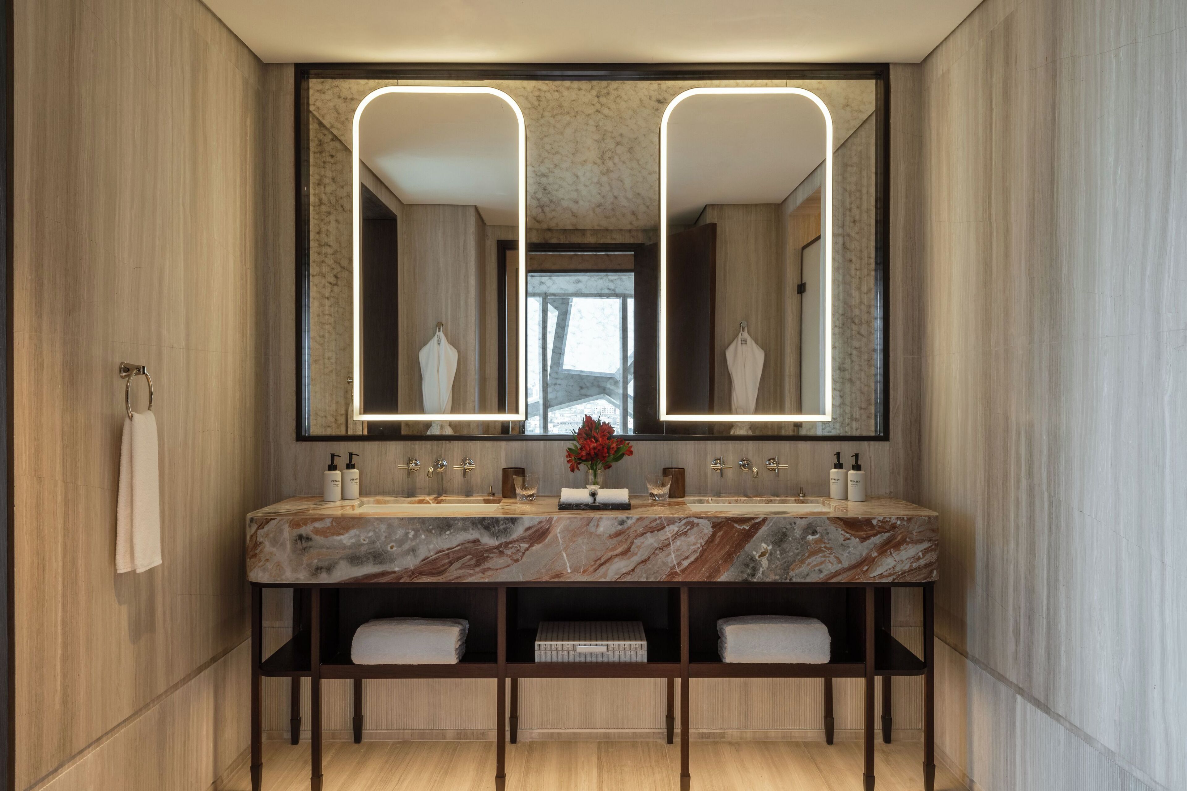 Un baño moderno con lavamanos de mármol, dos espejos y un mueble de tocador de madera.