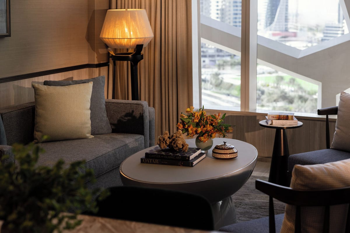 A modern living room with a sofa, a round coffee table, a lamp, and a view of the city through large windows.