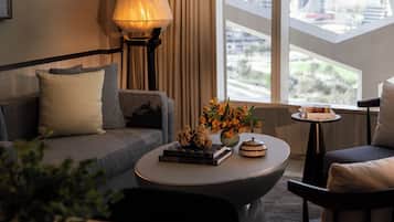 A modern living room with a sofa, a round coffee table, a lamp, and a view of the city through large windows.