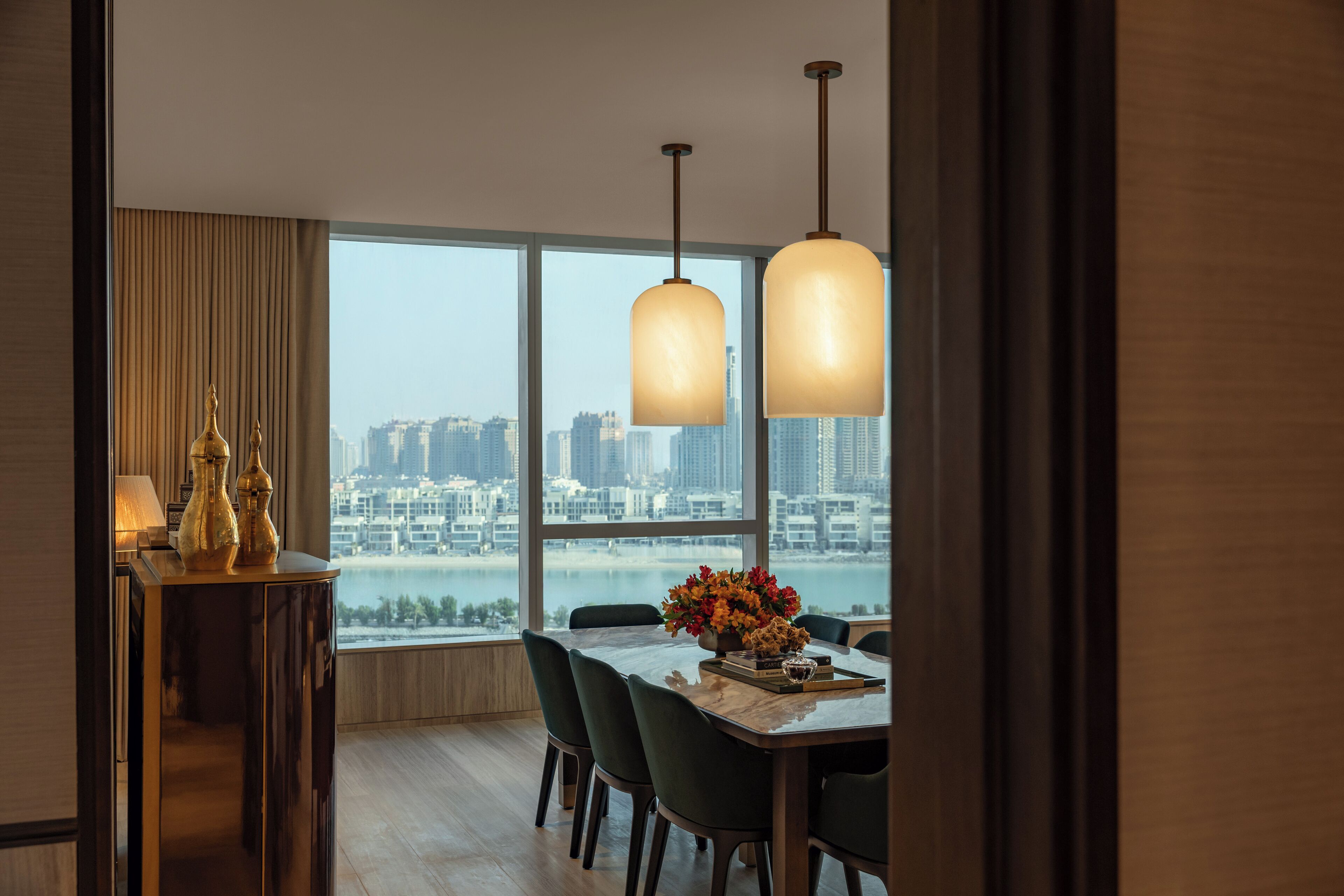 A dining area with a view of a cityscape through large windows, a wooden table, and modern pendant lights.