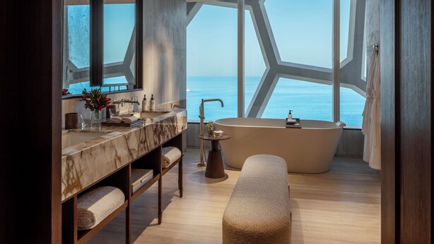 A modern bathroom with a marble vanity, a freestanding bathtub, and a bench. - Rosewood Doha (Doha)