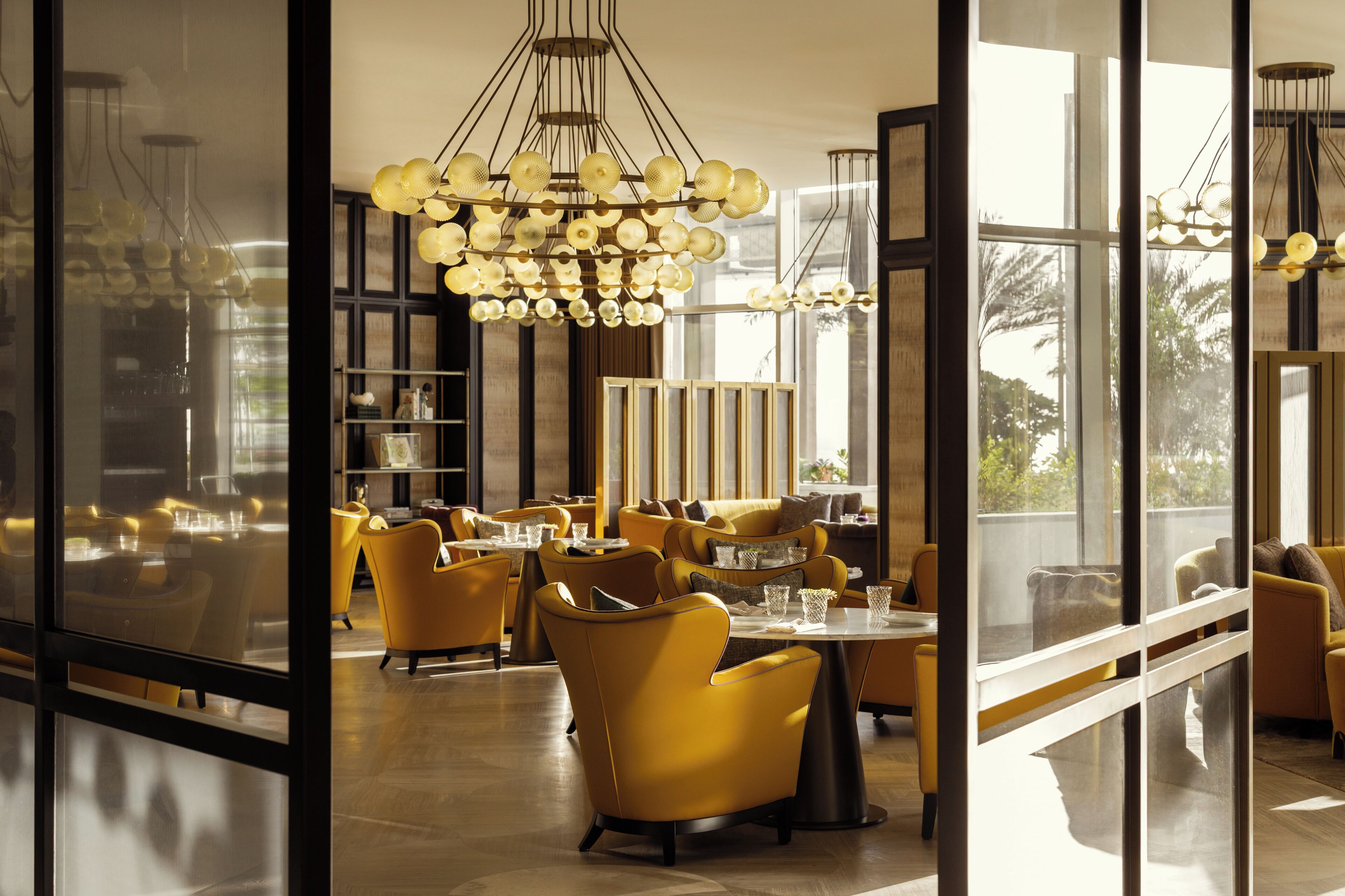 A modern interior with yellow chairs and tables, large windows, and a unique chandelier.