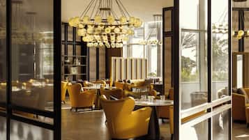 A modern interior with yellow chairs and tables, large windows, and a unique chandelier.
