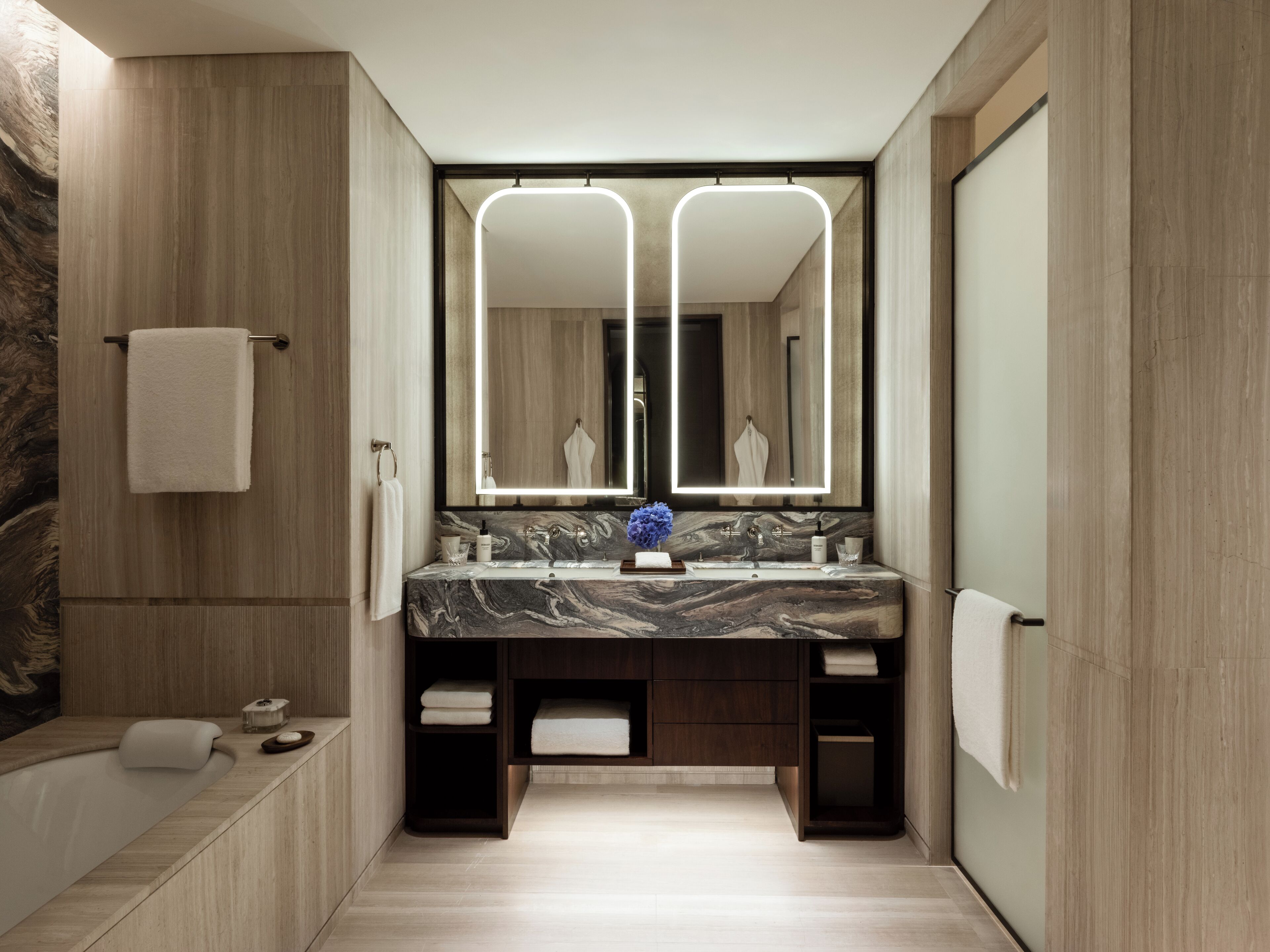 Un baño moderno con lavamanos de mármol, un espejo grande y muebles de madera.