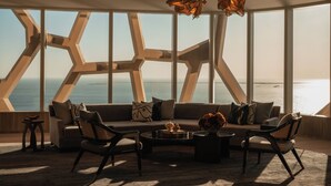 A modern living room with a large window overlooking the sea, a sectional sofa, two armchairs, a coffee table, and decorative lamps. - Rosewood Doha (Doha)