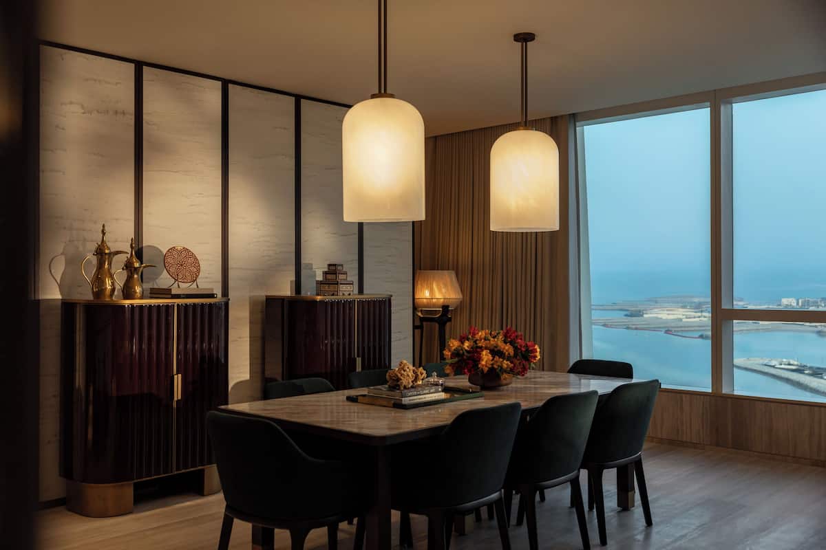 A modern dining area with a large table, chairs, and a view of a body of water through large windows.