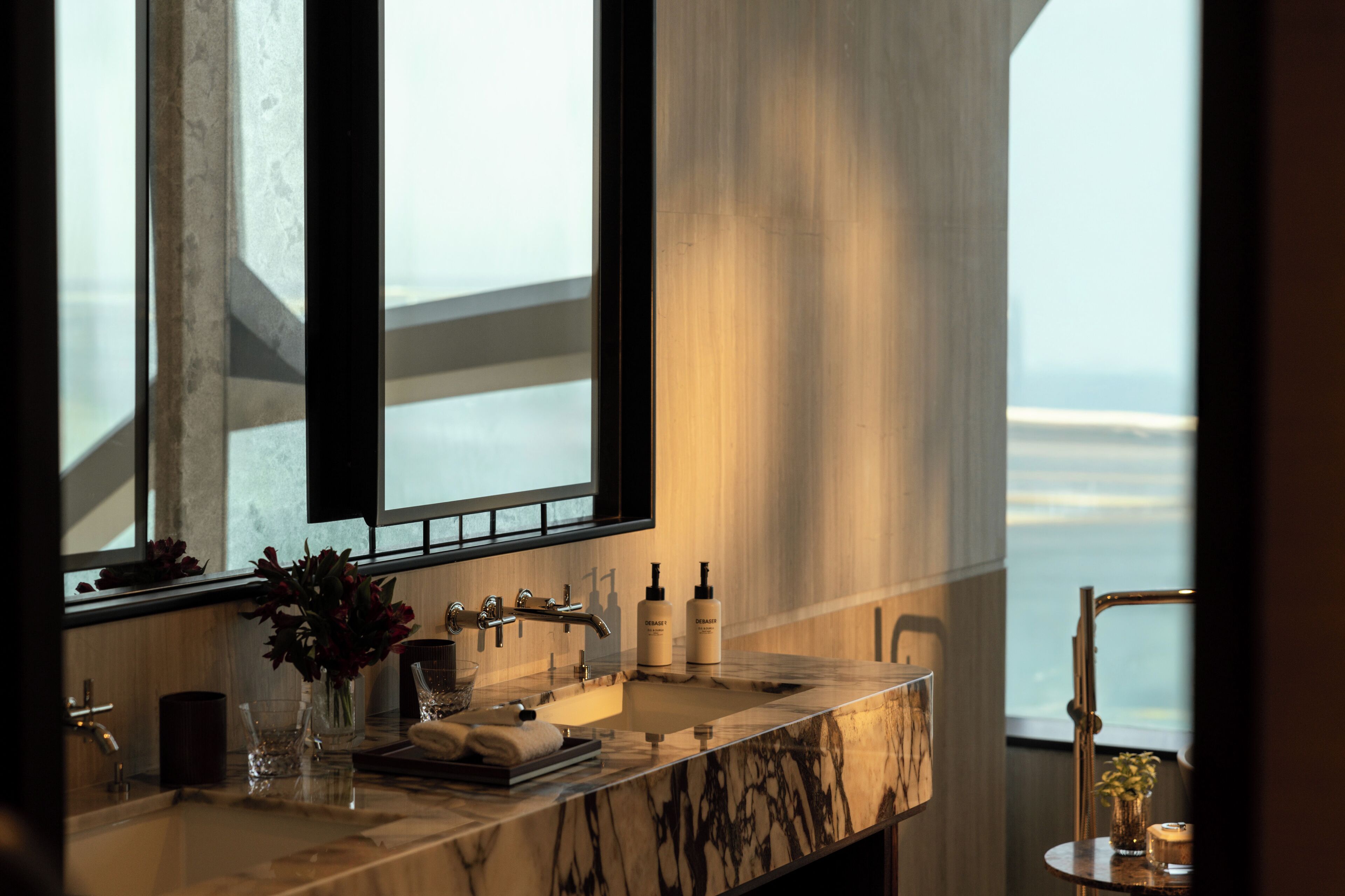 A modern bathroom with a marble sink, large windows, and a view of the sea.