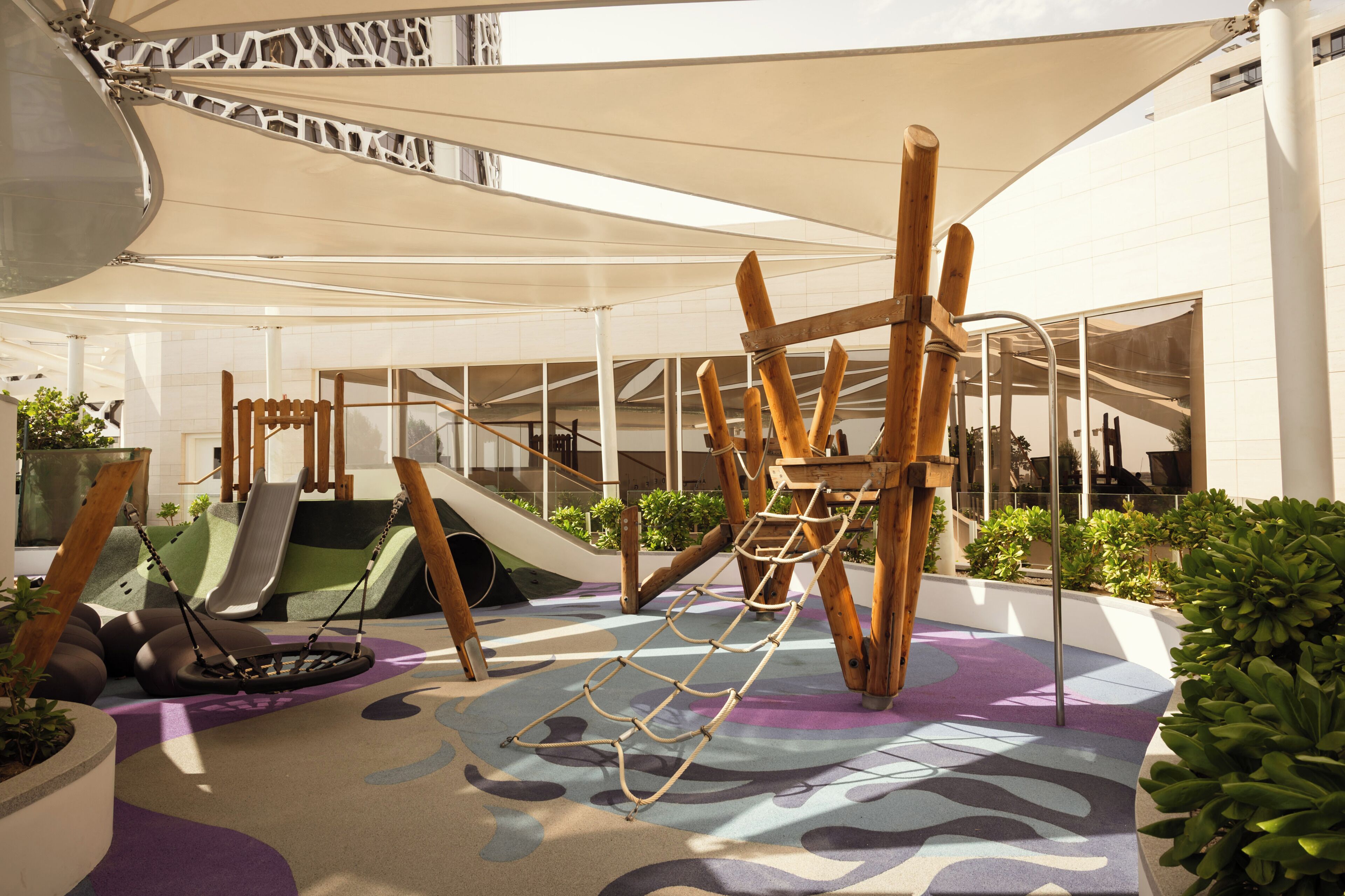 Un espace de jeux intérieur avec un toboggan, des balançoires et des structures d’escalade.
