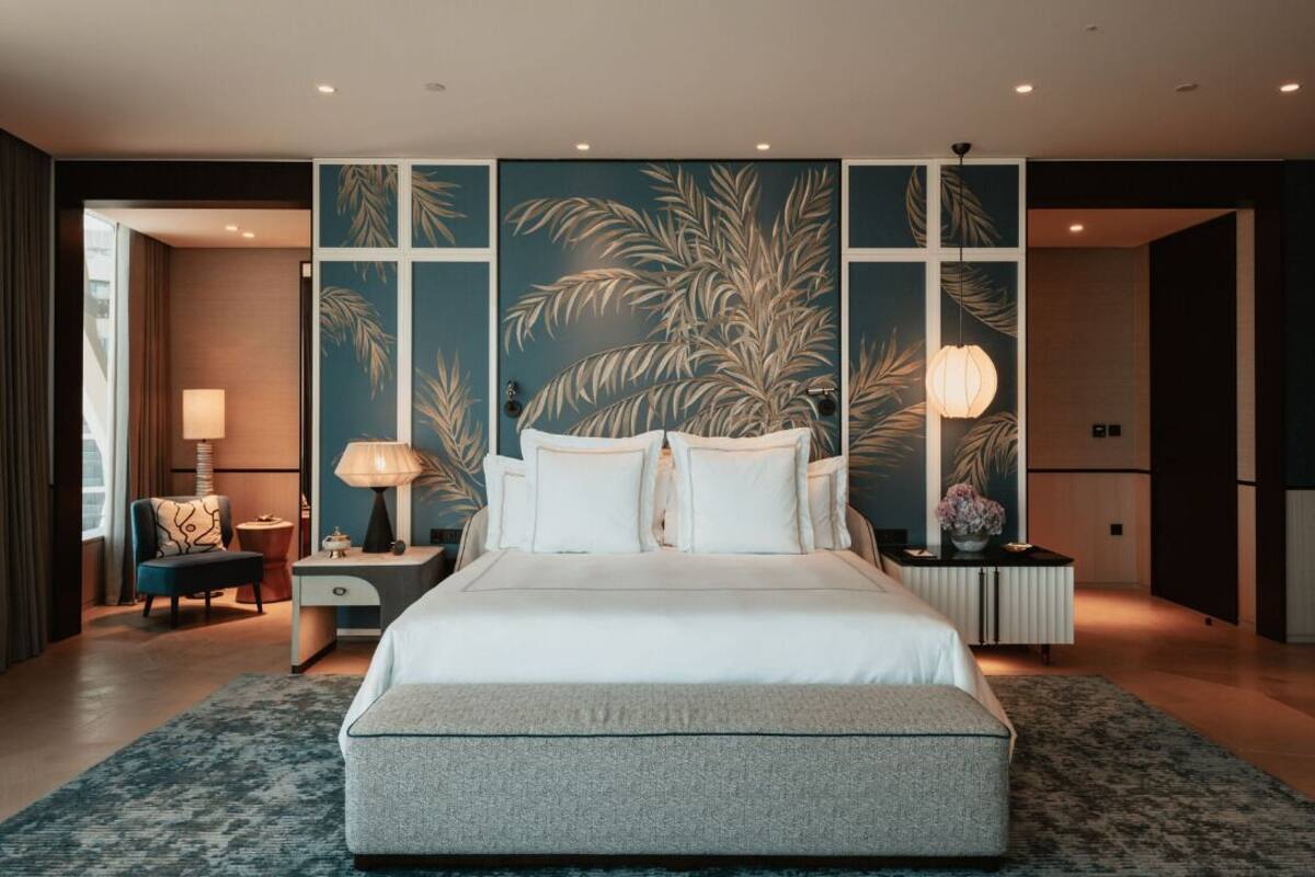 A modern hotel room with a large bed, a nightstand, a lamp, and a view of the hallway.