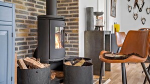 Een moderne woonkamer met een zwart houtvuuroven, een bakstenen muur en een leren fauteuil.