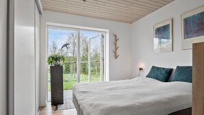 Een slaapkamer met een groot bed, een potplant, een houten kapstok en een lijst met een foto aan de muur.