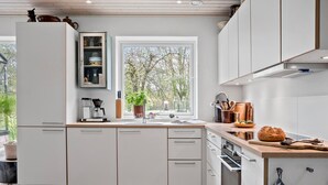 Een moderne keuken met witte kasten, een inbouwoven, een koffiezetapparaat en een raam met uitzicht op bomen.