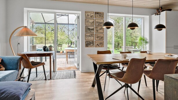 Een ruime eetruimte met een houten tafel en stoelen, grote ramen met kunstwerken, en uitzicht op de tuin.