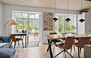 Un comedor amplio con una mesa y sillas de madera, ventanas grandes con obras de arte y vistas al jardín.