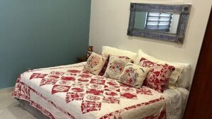 A bedroom with a bed covered in a floral-patterned bedspread, a small rug, and a mirror on the wall. - Beautiful Condo with view of the city, mountain & partial Oceanview.  (Playa de oro Zona Hotelera. Nte.c p)