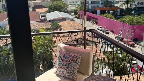 A balcony with a red umbrella, a sofa with a patterned pillow, and a small round table. - Beautiful Condo with view of the city, mountain & partial Oceanview.  (Playa de oro Zona Hotelera. Nte.c p)