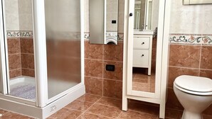 Ein Badezimmer mit einer gläsernen Duschkabine, einer weißen Toilette, einem Waschtisch mit Spiegel und einem Fliesenboden.