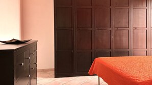 Ein Zimmer mit einem dunklen Holzschrank, einer schwarzen Kommode mit Schubladen und einem Bett mit orangefarbener Bettdecke.
