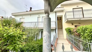 Ein Wohngebäude mit Balkon, Treppe und einer 3 auf einem Pfeiler.