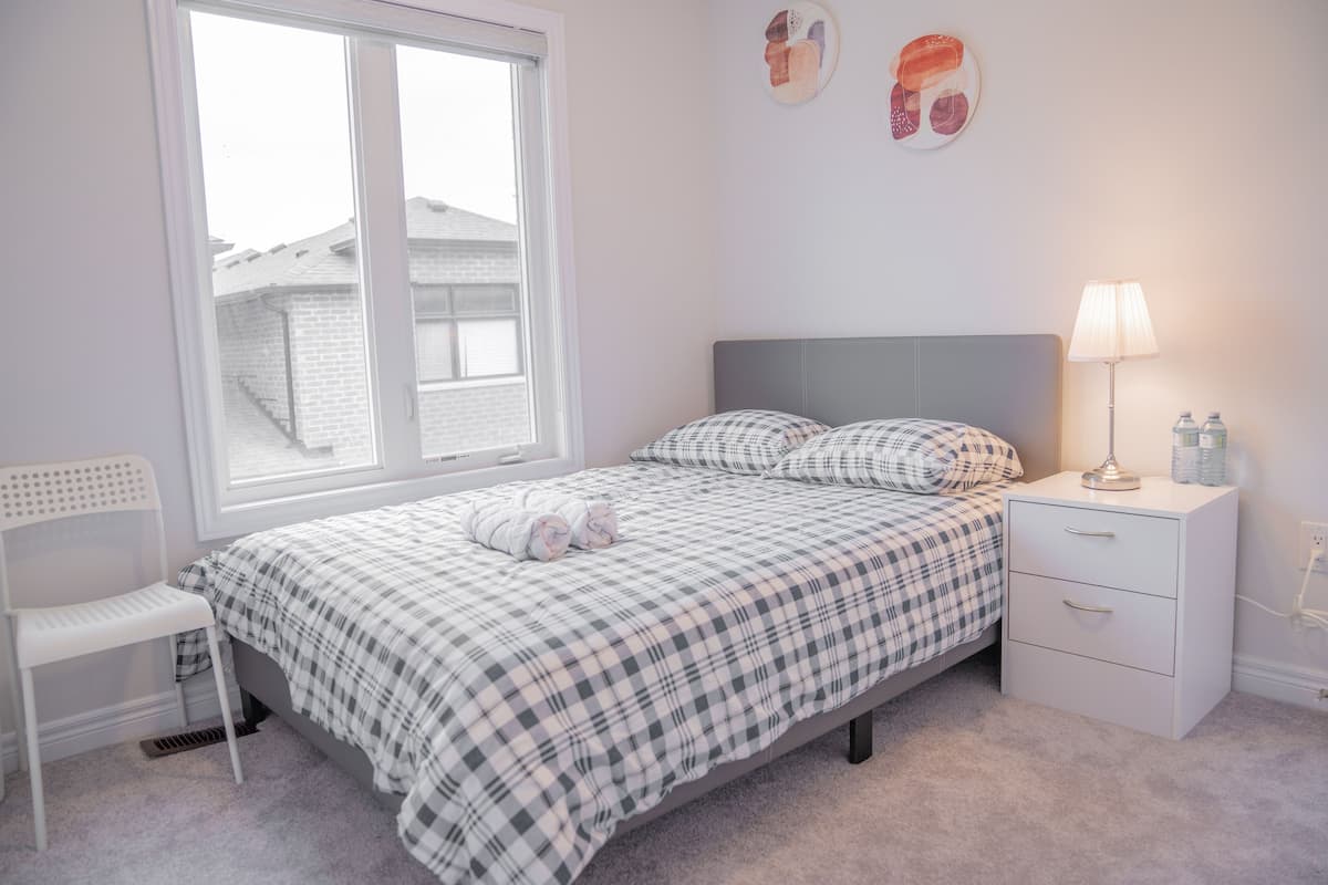 Ein Schlafzimmer mit einem Bett, einem Nachttisch mit Lampe, einem Sessel und einem Fenster.