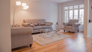 En stue med en beige sofa, en matchende lænestol og et sofabord i glas.