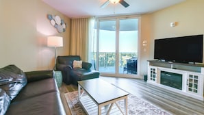 A living room with a sofa, armchair, coffee table, TV, and a balcony with a view. - Salted Tranquility at The Palms Of Destin (Destin)