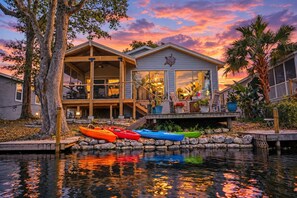 Ein Wassergrundstück mit Holzterrasse, Kajaks und einem Haus mit großen Fenstern.