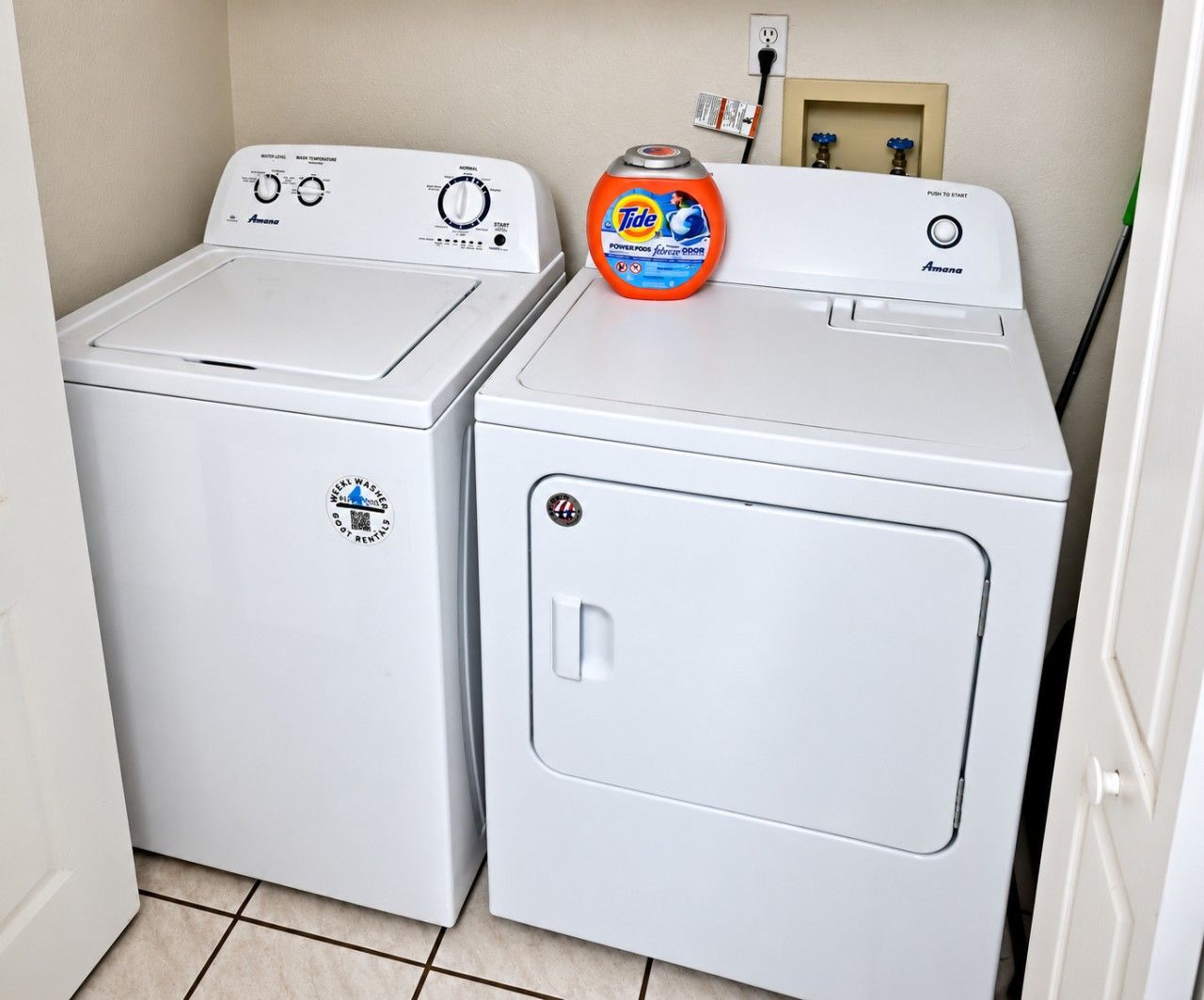 Two white front-loading washing machines in a laundry room with a Tide detergent bottle on top of the right machine.