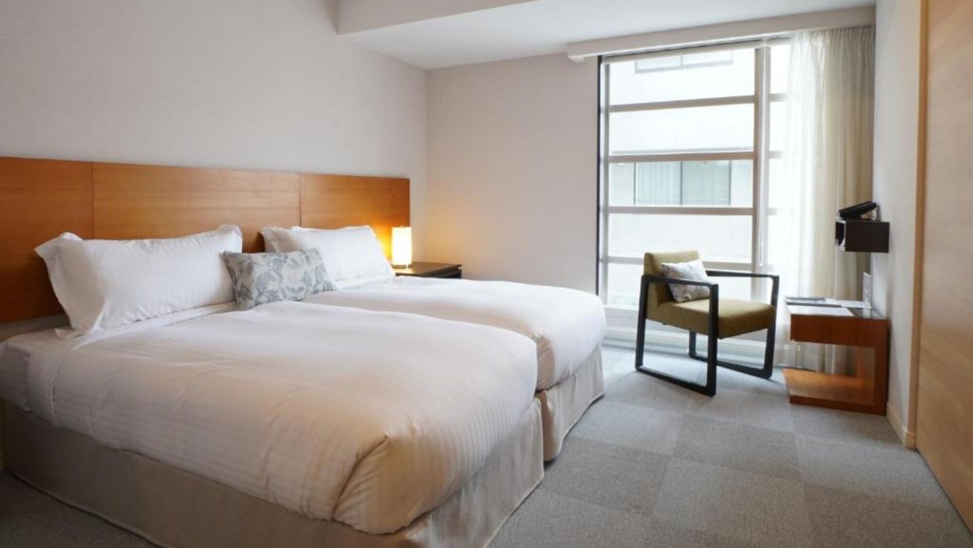 A hotel room with two beds, a chair, a desk, and a large window.