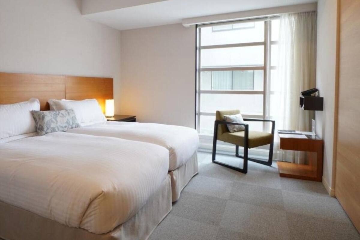 Habitación de hotel con dos camas, una silla, un escritorio y un ventanal grande.