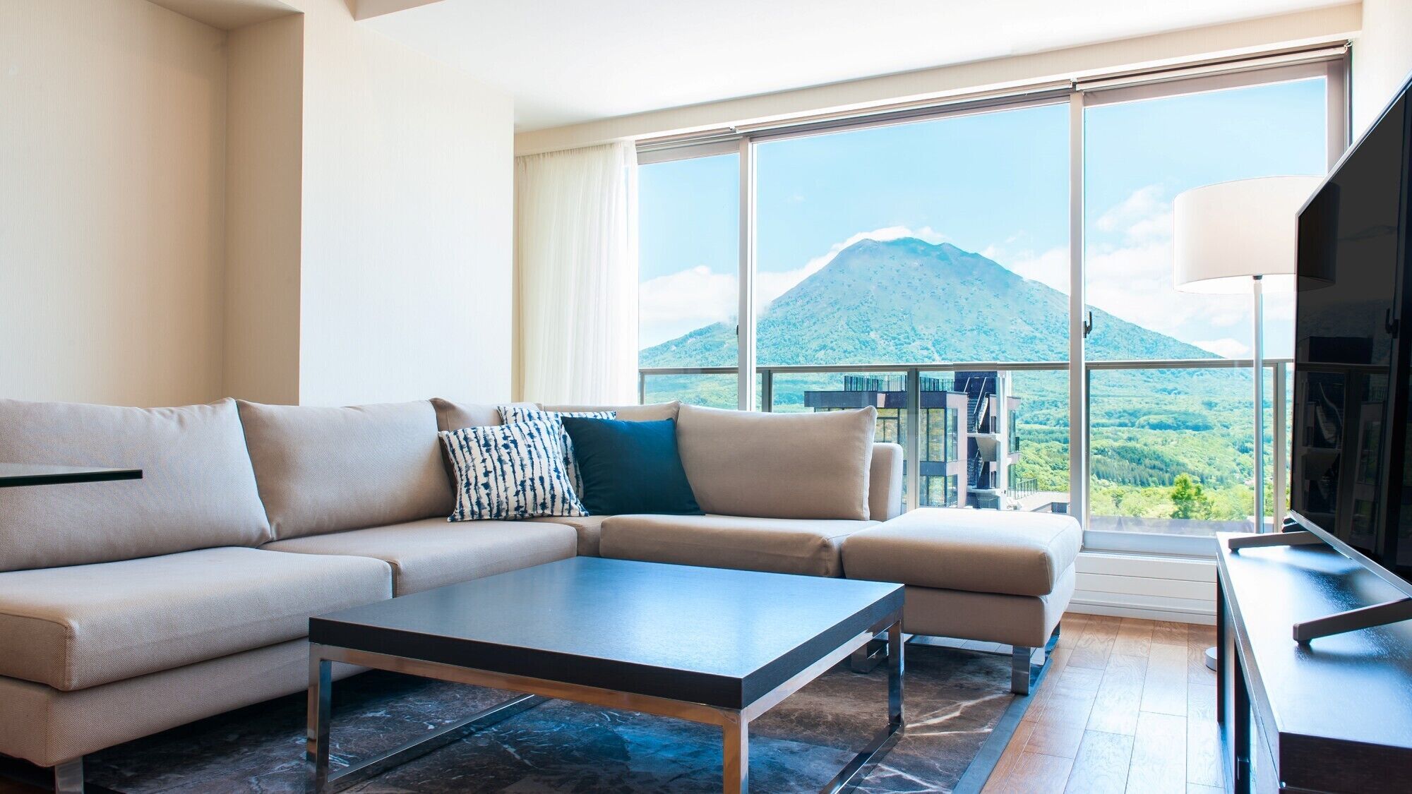 A modern living room with a sofa, coffee table, and a large window offering a mountain view.