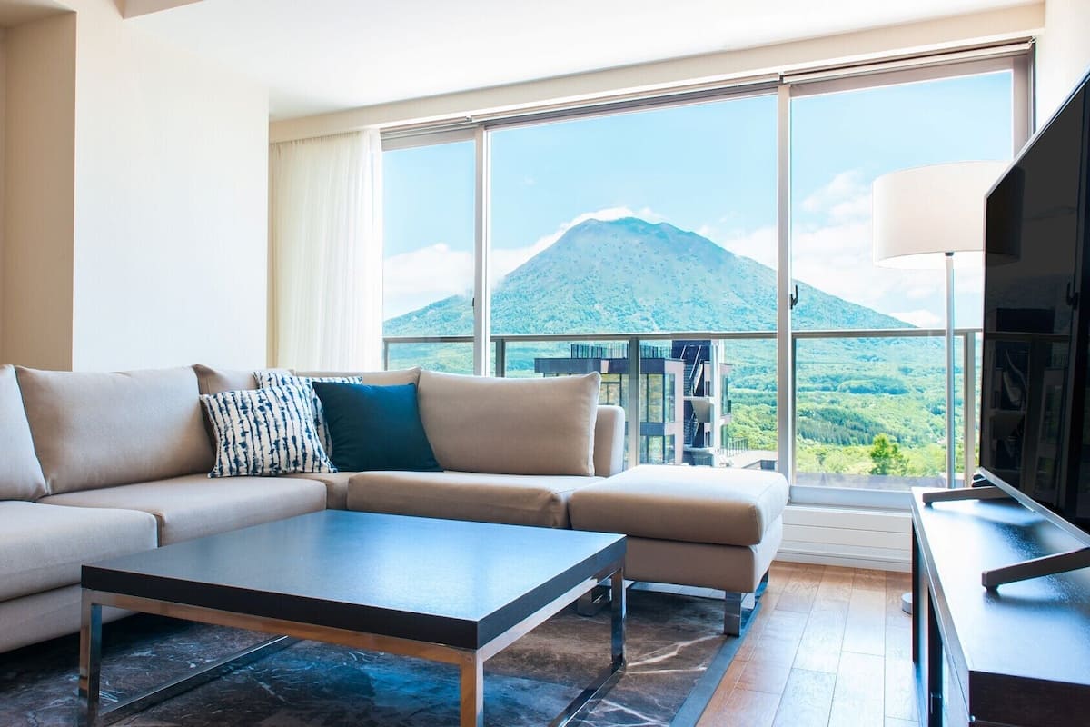 Una sala de estar moderna con un sofá, una mesa de centro y un ventanal con vistas a la montaña.