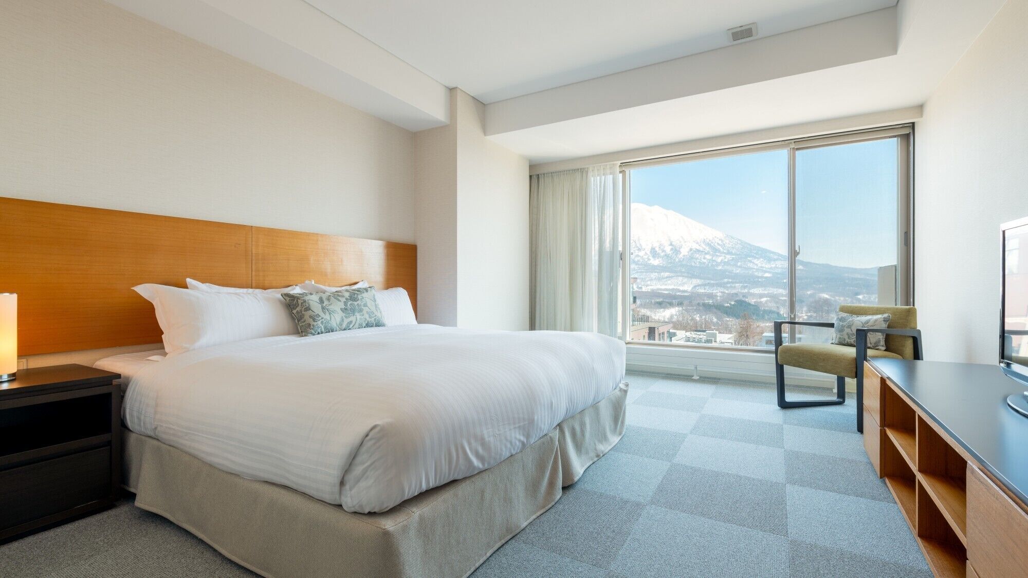 A hotel room with a large bed, a desk, a chair, and a view of a mountain.