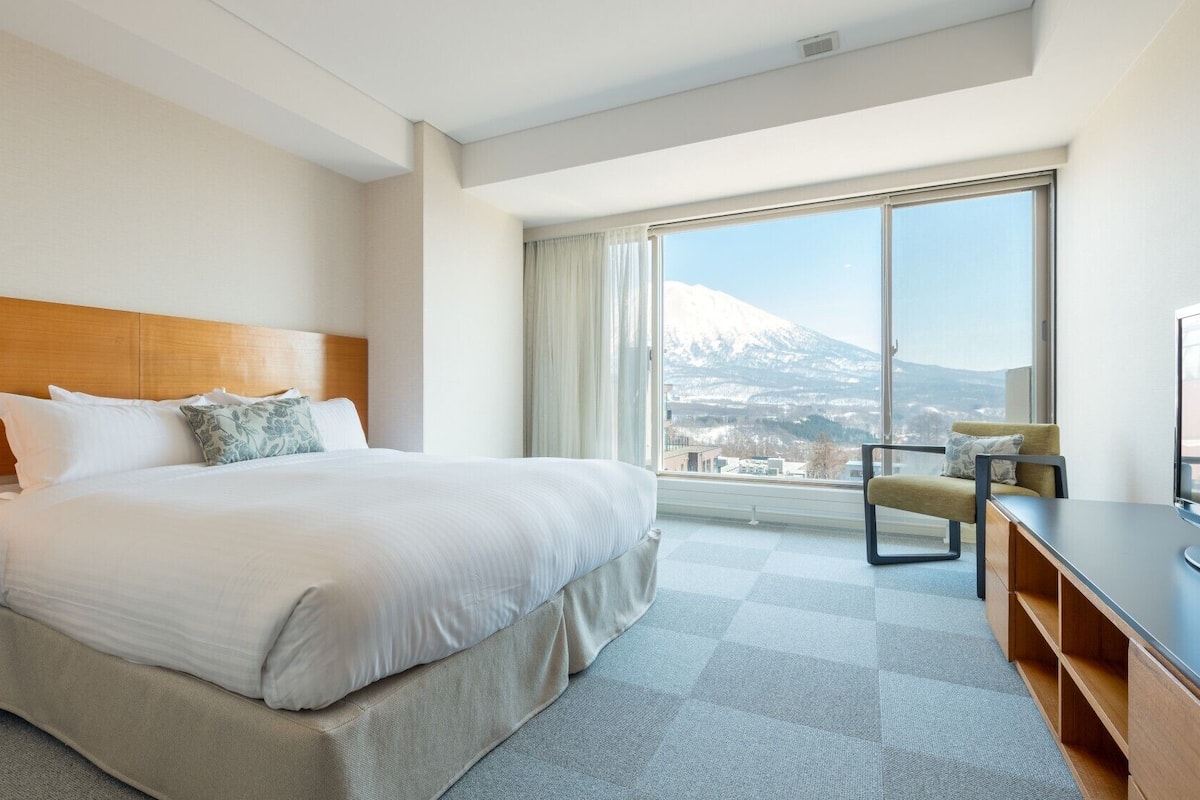 Habitación de hotel con una cama grande, un escritorio, una silla y vistas a la montaña.